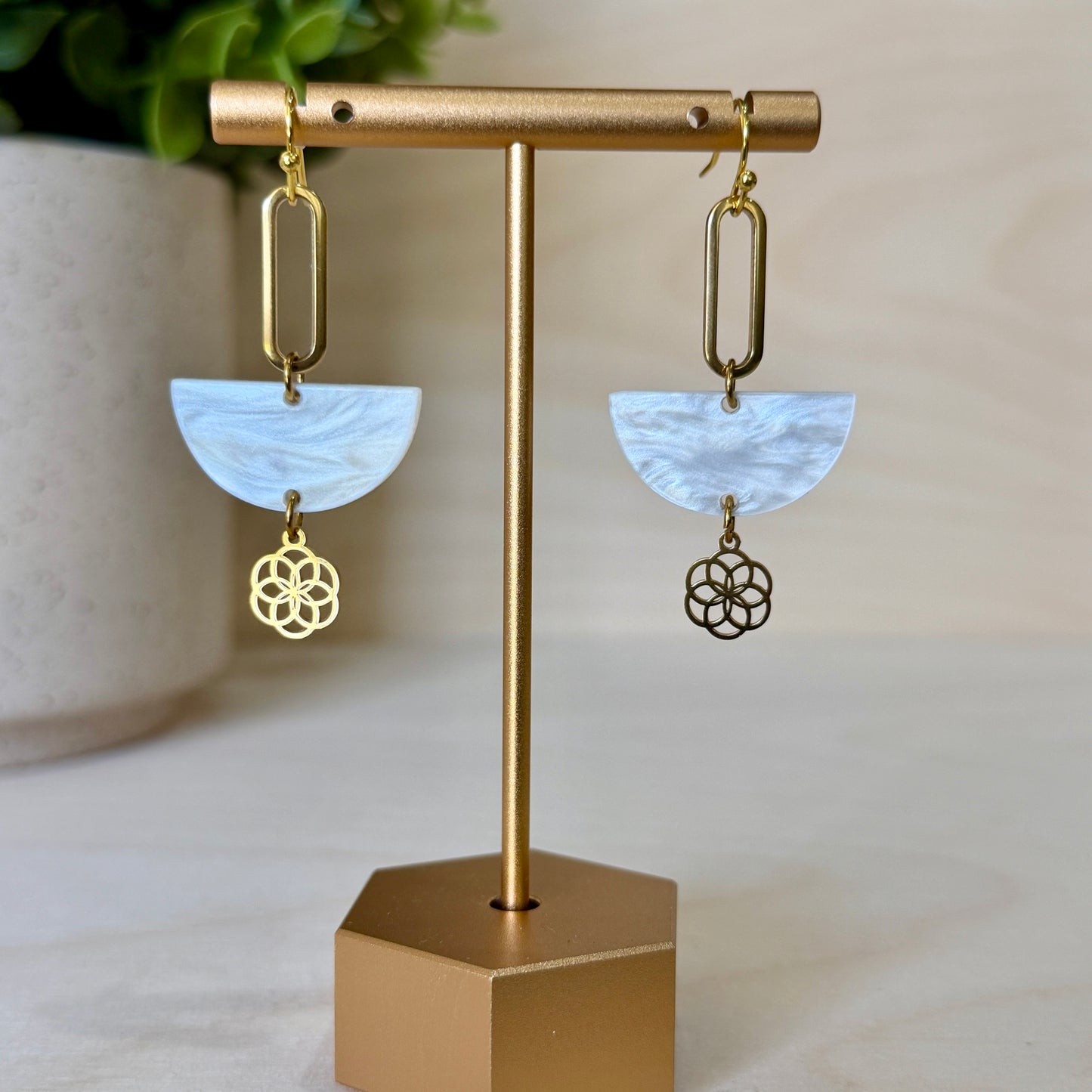 Gold earrings with white stone and floral design on a gold stand against a neutral background