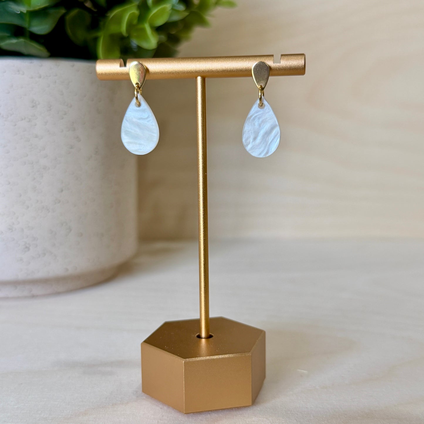 Gold earring stand with teardrop-shaped earrings in front of a potted plant.