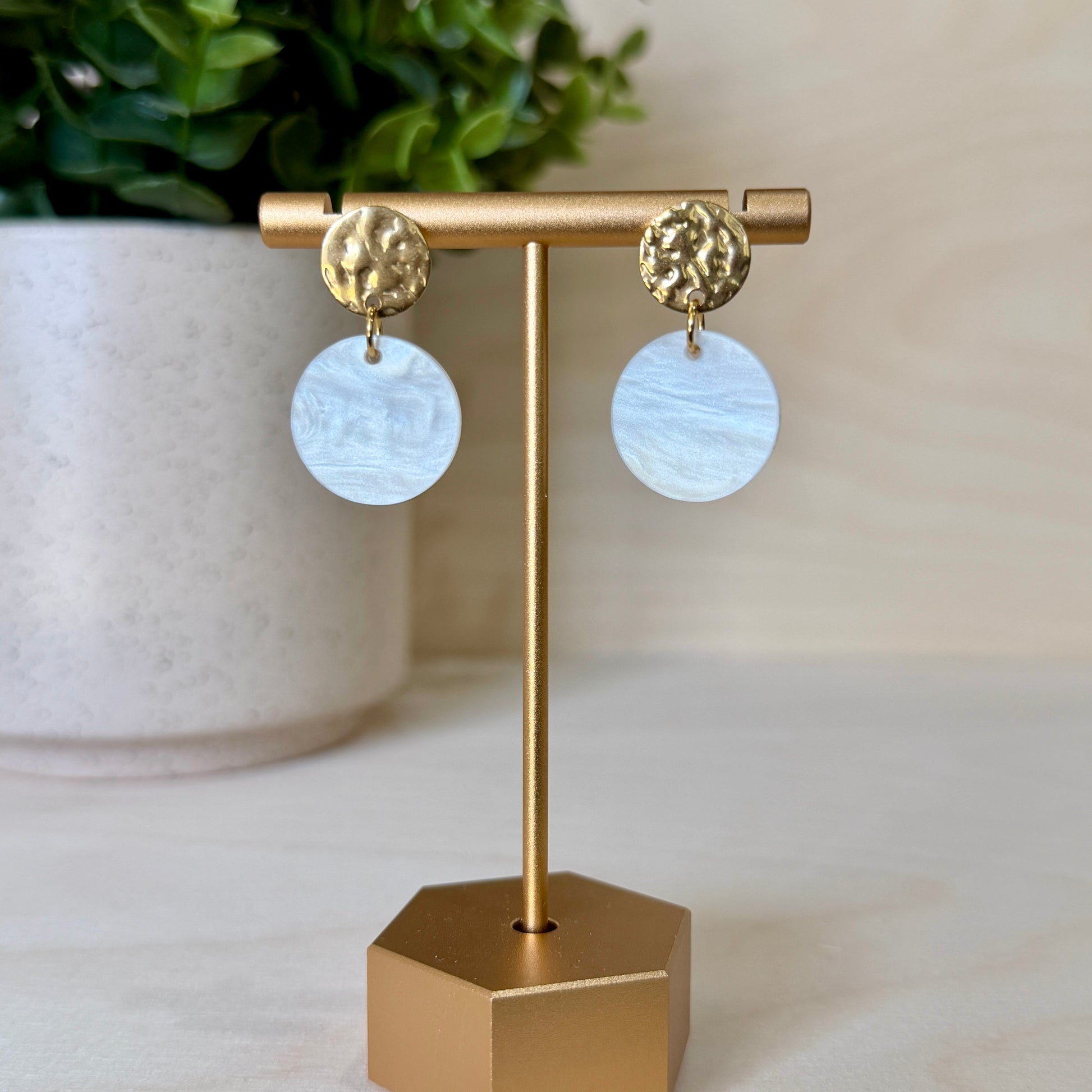 Gold earrings with round, light blue stones on a gold stand against a neutral background.