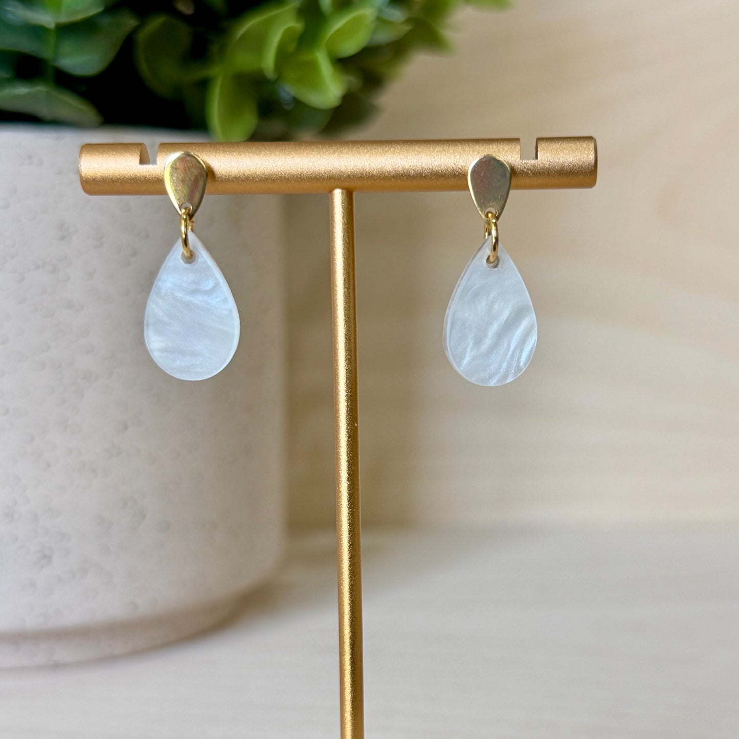 Teardrop-shaped earrings on a gold earring stand with a blurred plant in the background