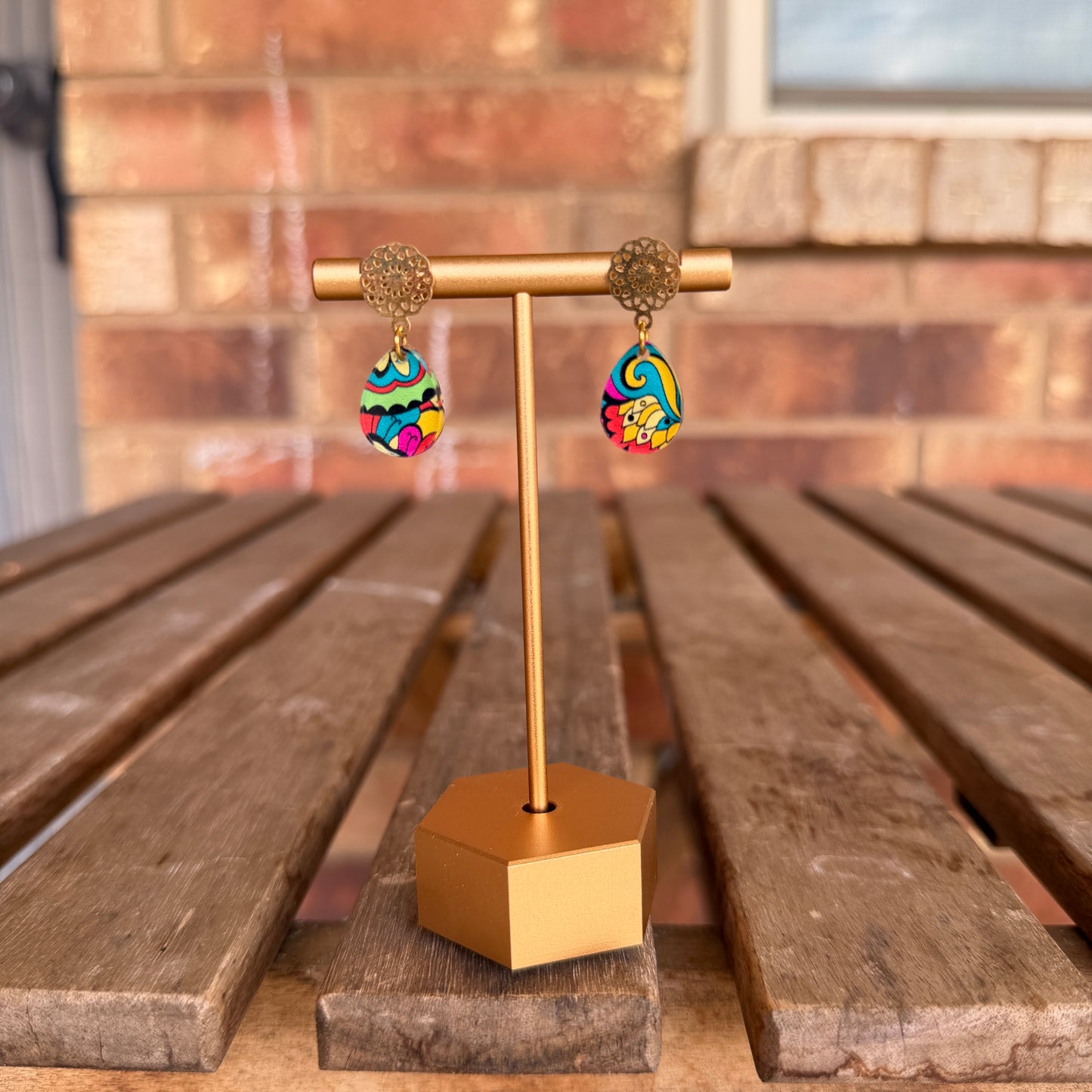 Colorful earrings on a gold earring stand against a brick wall background