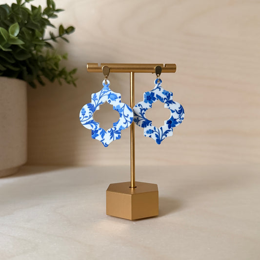 Blue floral earrings on a gold stand with a beige background