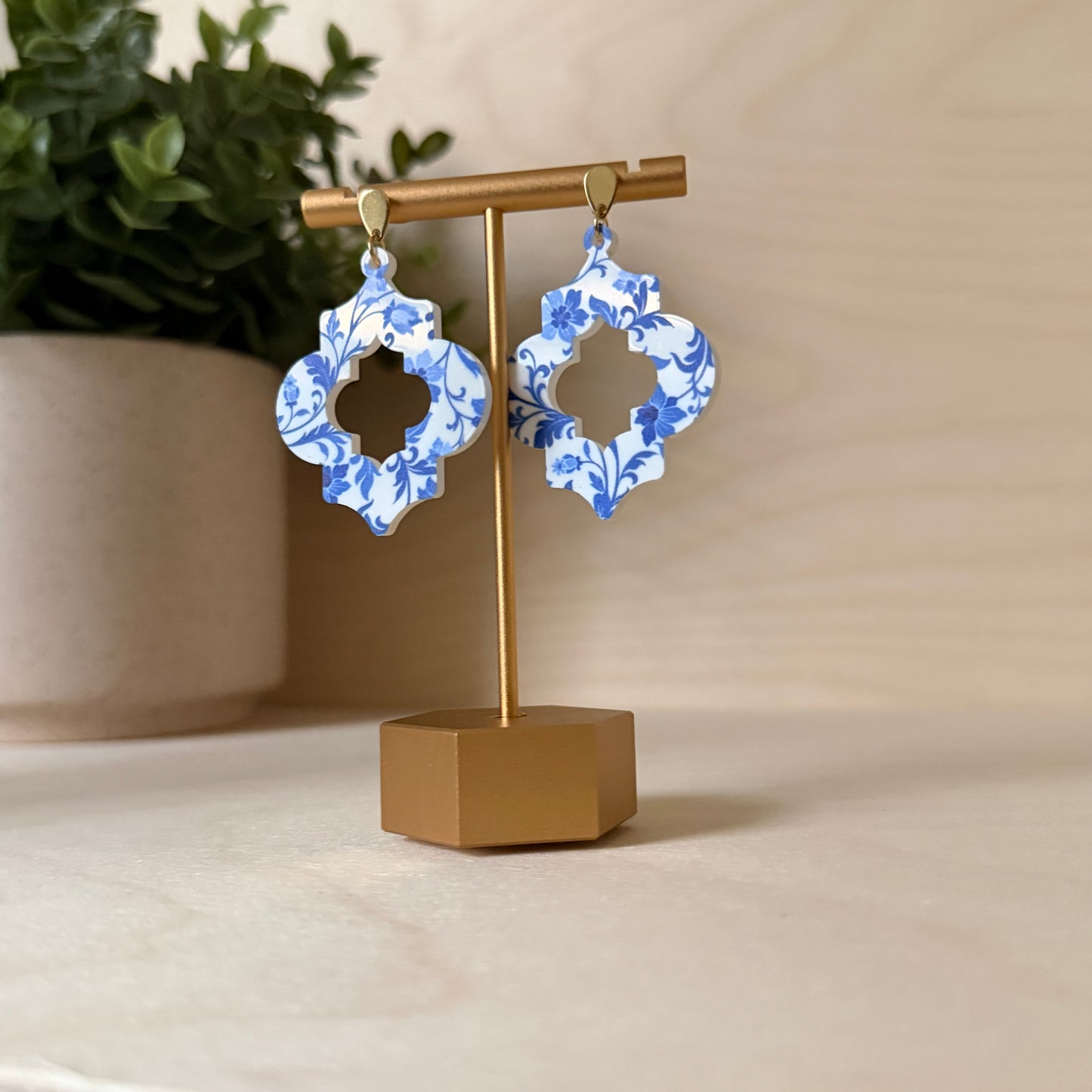 Blue and white floral earrings on a gold stand with a beige background