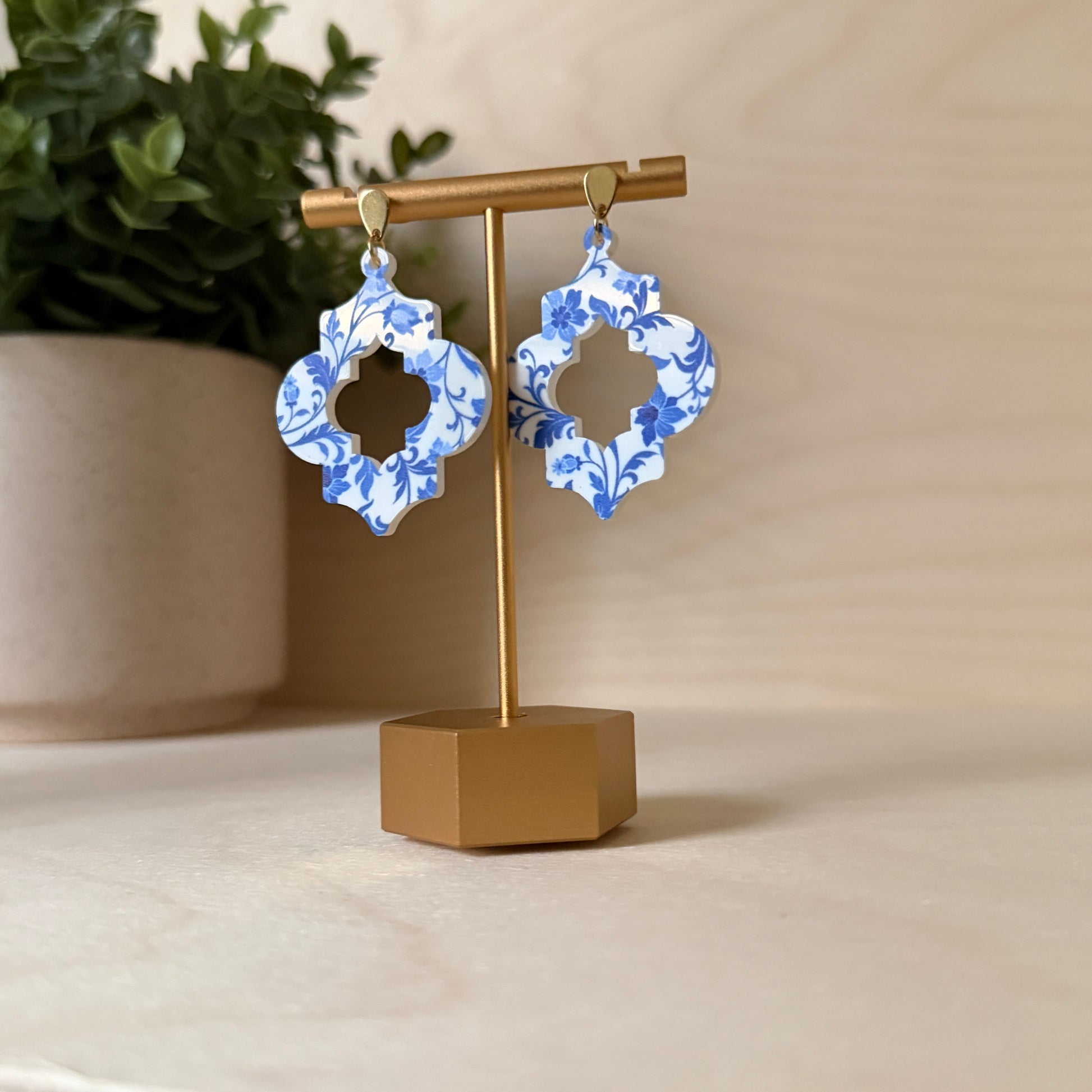 Blue and white floral earrings on a gold stand with a beige background