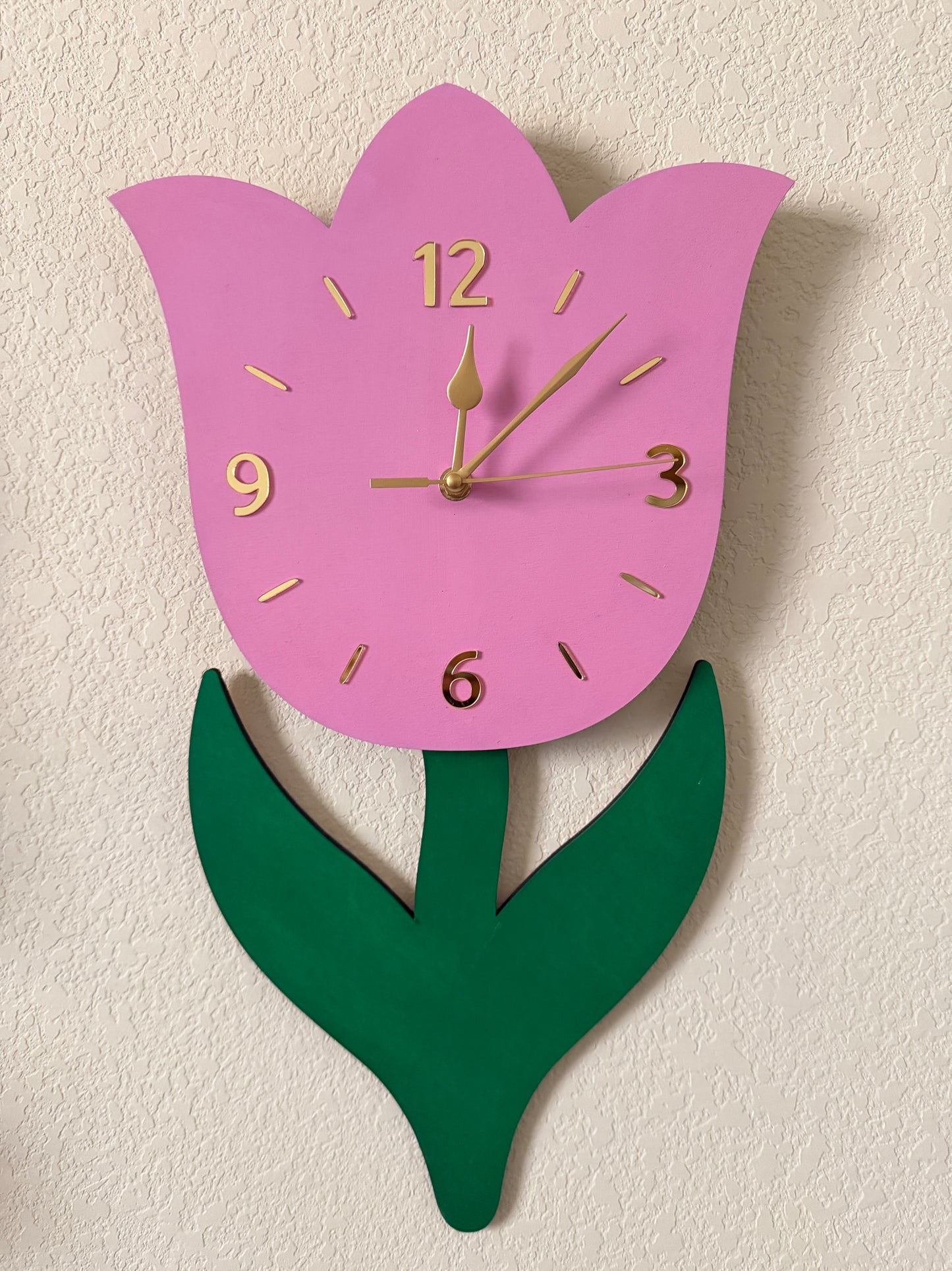 Pink tulip-shaped clock with a green leaf on a beige background