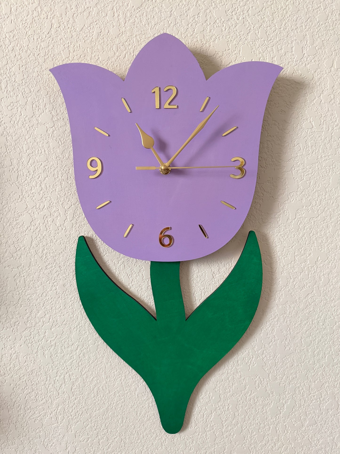 Decorative wall clock shaped like a tulip with purple petal and green leaf on a textured white background