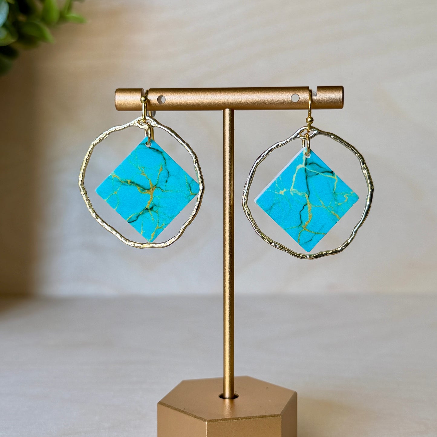 Turquoise earrings with gold accents on a gold stand against a neutral background