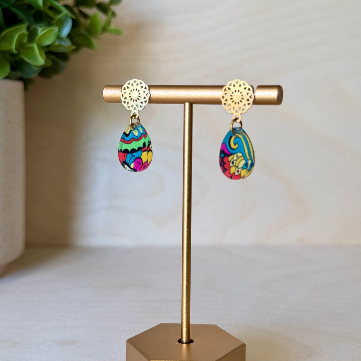 Colorful earrings on a gold earring stand with a plant in the background