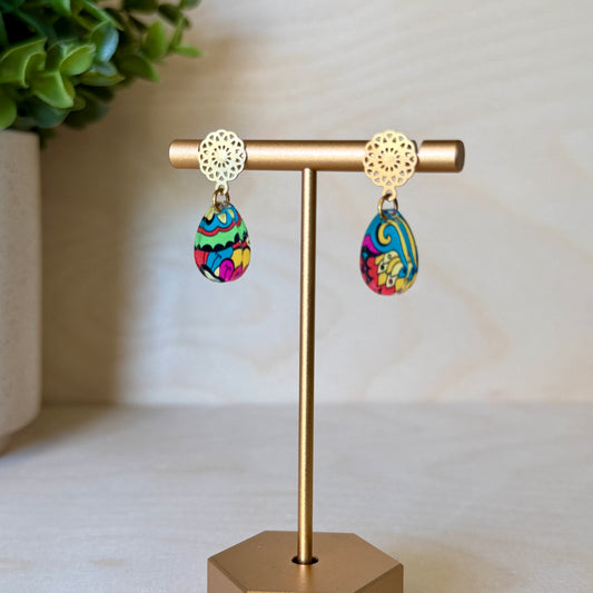 Colorful earrings on a gold earring stand with a plant in the background