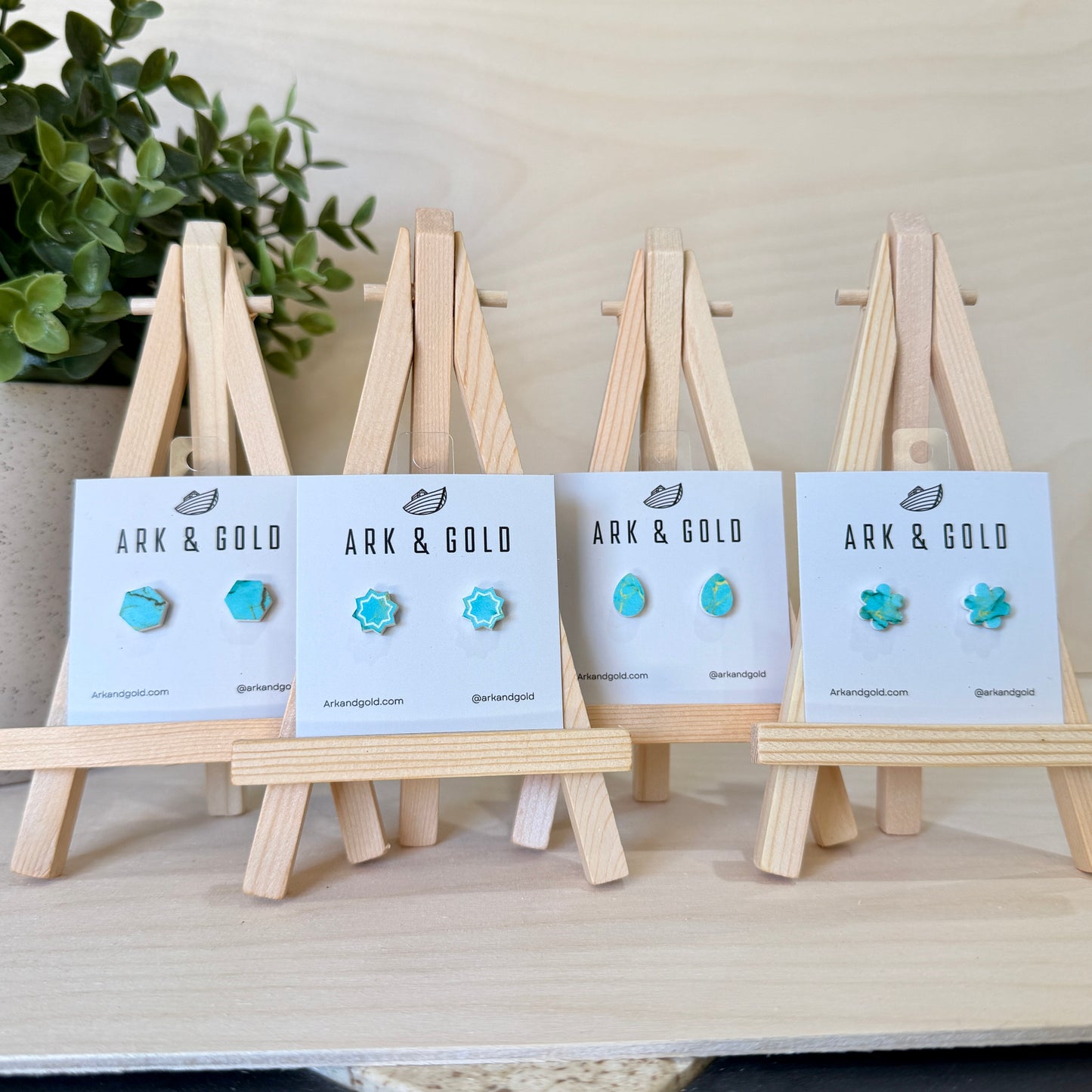 Turquoise earrings on display with 'ARK & GOLD' cards on wooden stands.