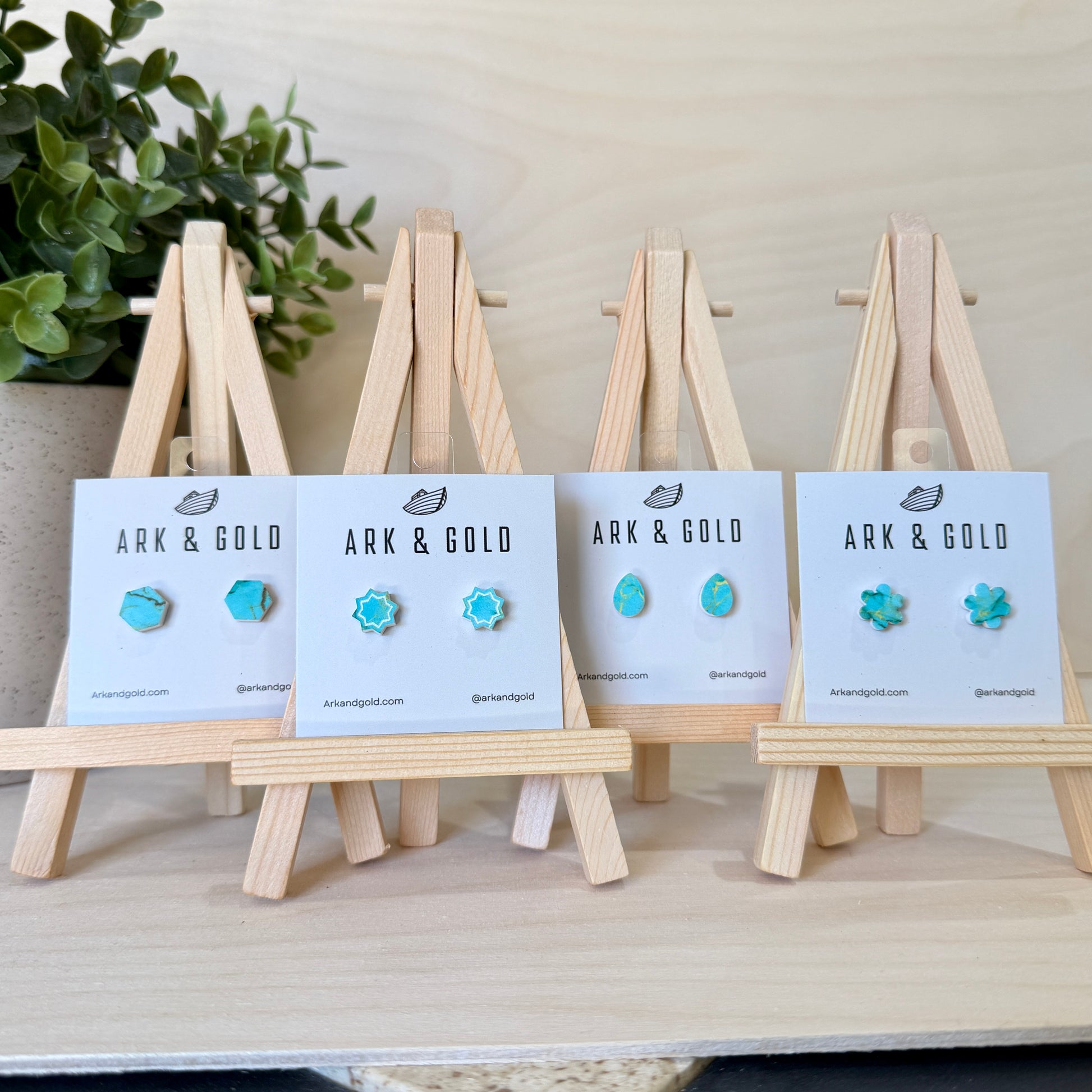 Turquoise earrings on display with 'ARK & GOLD' cards on wooden stands.