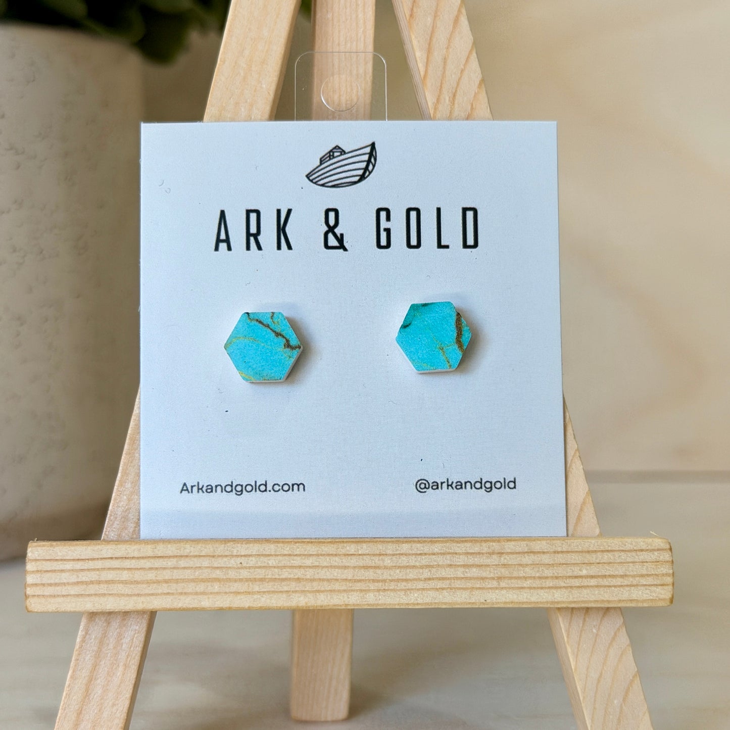 Turquoise hexagonal earrings on an Ark & Gold branded card with a wooden stand.