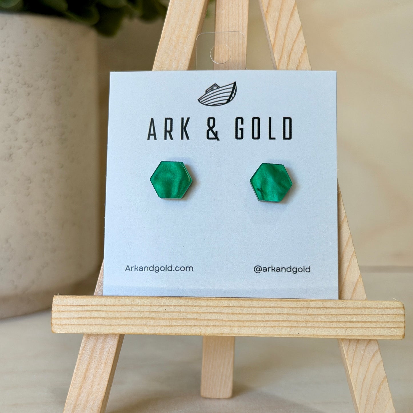 Green geometric earrings on a 'ARK & GOLD' branded card with a wooden stand.