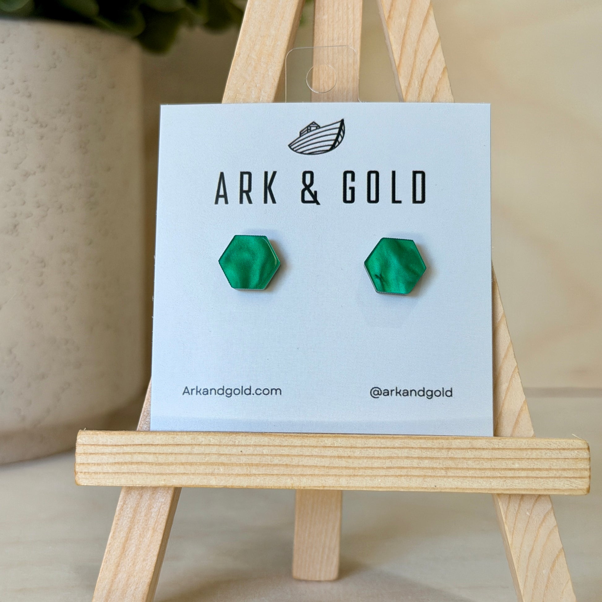 Green geometric earrings on a 'ARK & GOLD' branded card with a wooden stand.