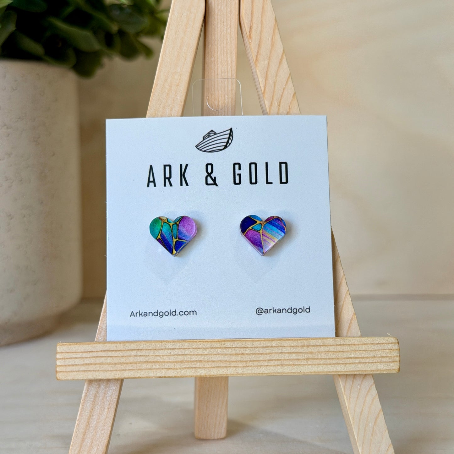 Heart-shaped earrings on a 'ARK & GOLD' branded card with a wooden stand.