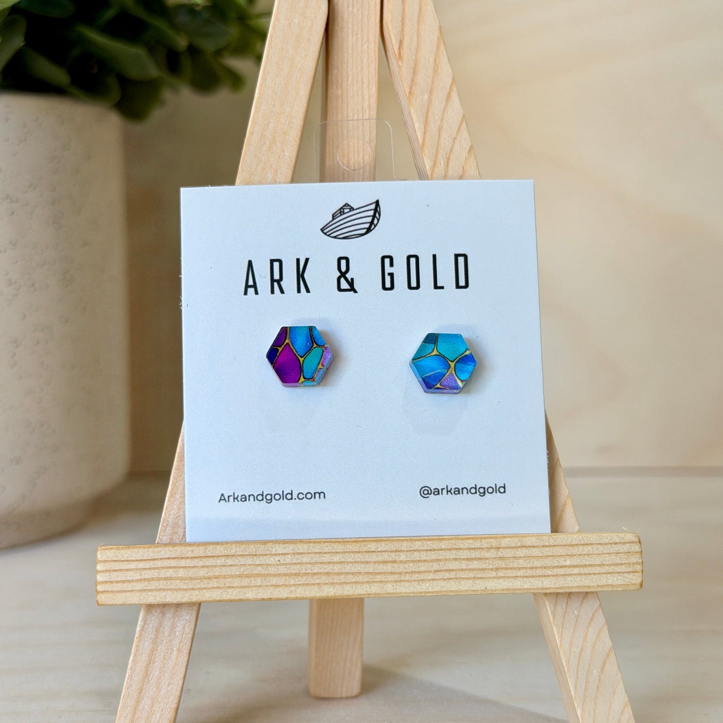 Ark & Gold hexagon stud earrings on a display card with a wooden stand.
