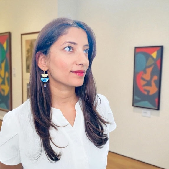 Woman in a white shirt standing in an art gallery with colorful abstract paintings on the wall.